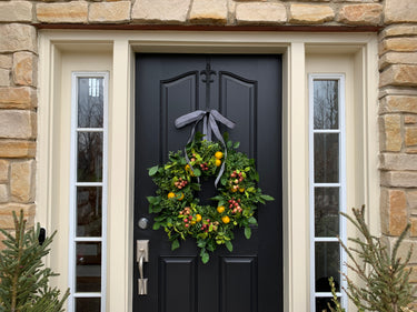 front view of Lemon, crabapple and boxwood wreath with black and white striped ribbon on black front door